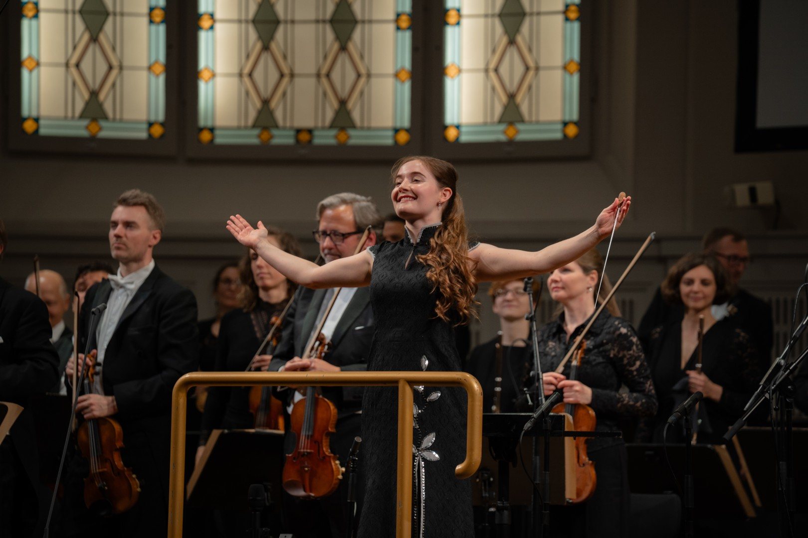 Alma Deutscher, arms outstretched, acknowledging the applause with the orchestra on stage